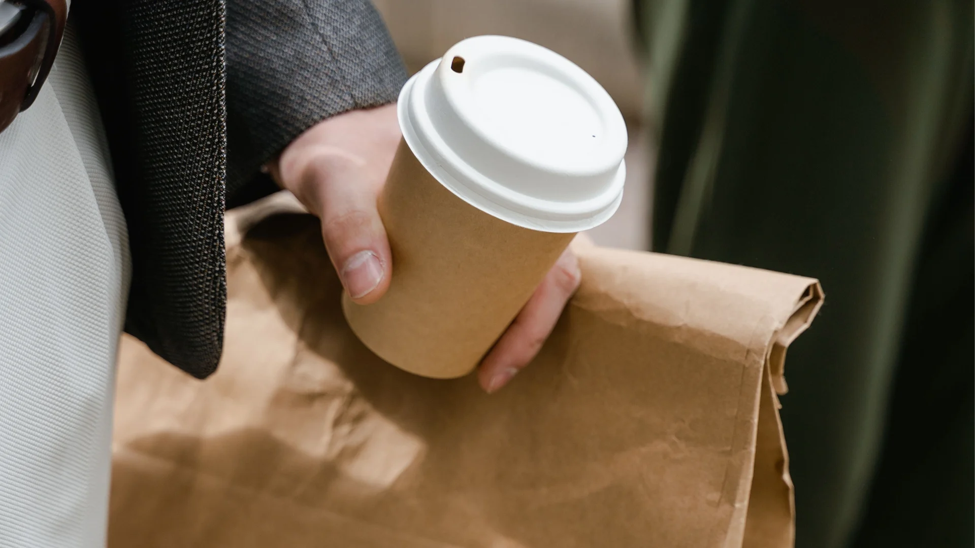 Barista predaje mušteriji dva kafea za poneti u nosaču za pića, sa papirnom kesom i salvetama na pultu kafića