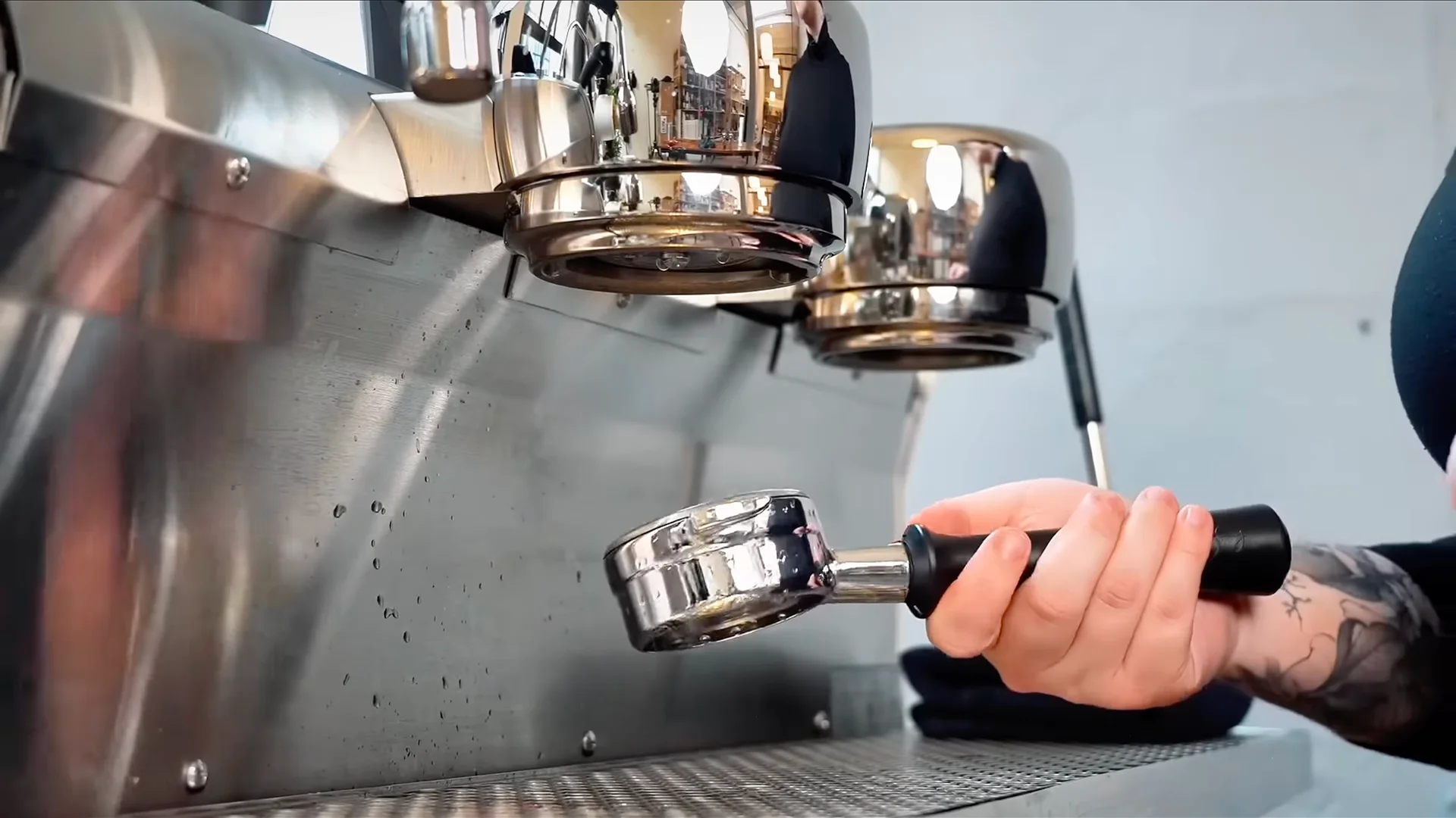 Barista u rukavicama čisti mlaznicu za paru espreso mašine u mernoj posudi sa sredstvom za čišćenje, krpom i četkom na šanku kafića